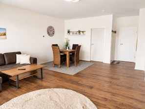 A living room with a sofa, a coffee table, a dining table with chairs, a clock, and a door.