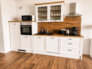 A compact kitchen with white cabinetry, a microwave, an oven, a coffee maker, and a wooden countertop.