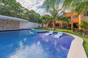 A swimming pool with a tiled edge, surrounded by a white wall and a grassy area with palm trees. - Villa Coral (Tulum)