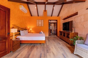 A bedroom with a bed, bedside tables, a TV, and a seating area with a chair. - Villa Coral (Tulum)