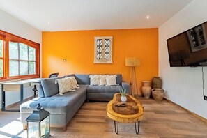 A modern living room with a grey sectional sofa, a wooden coffee table, and a large window with red blinds. - Villa Coral (Tulum)