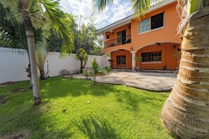 A two-story building with a balcony, surrounded by a well-maintained lawn and palm trees. - Villa Coral (Tulum)