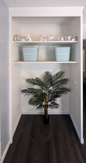Een hoekkast met planken, waarop 'OCEAN SEA Beach' staat, en een potpalm.