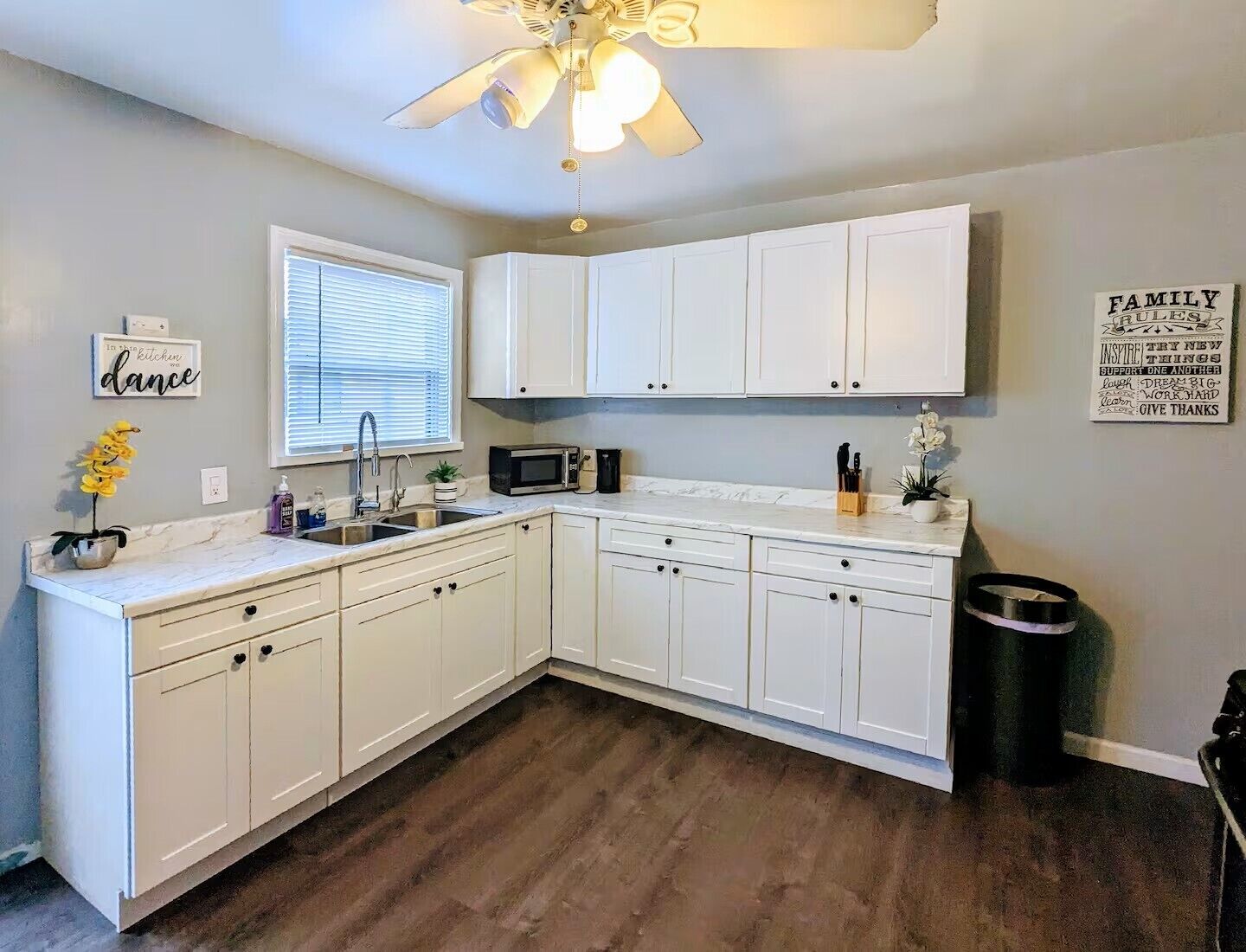 A kitchen with white cabinets, a microwave, a sink, and a ceiling fan.