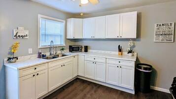 A kitchen with white cabinets, a microwave, a sink, and a ceiling fan.