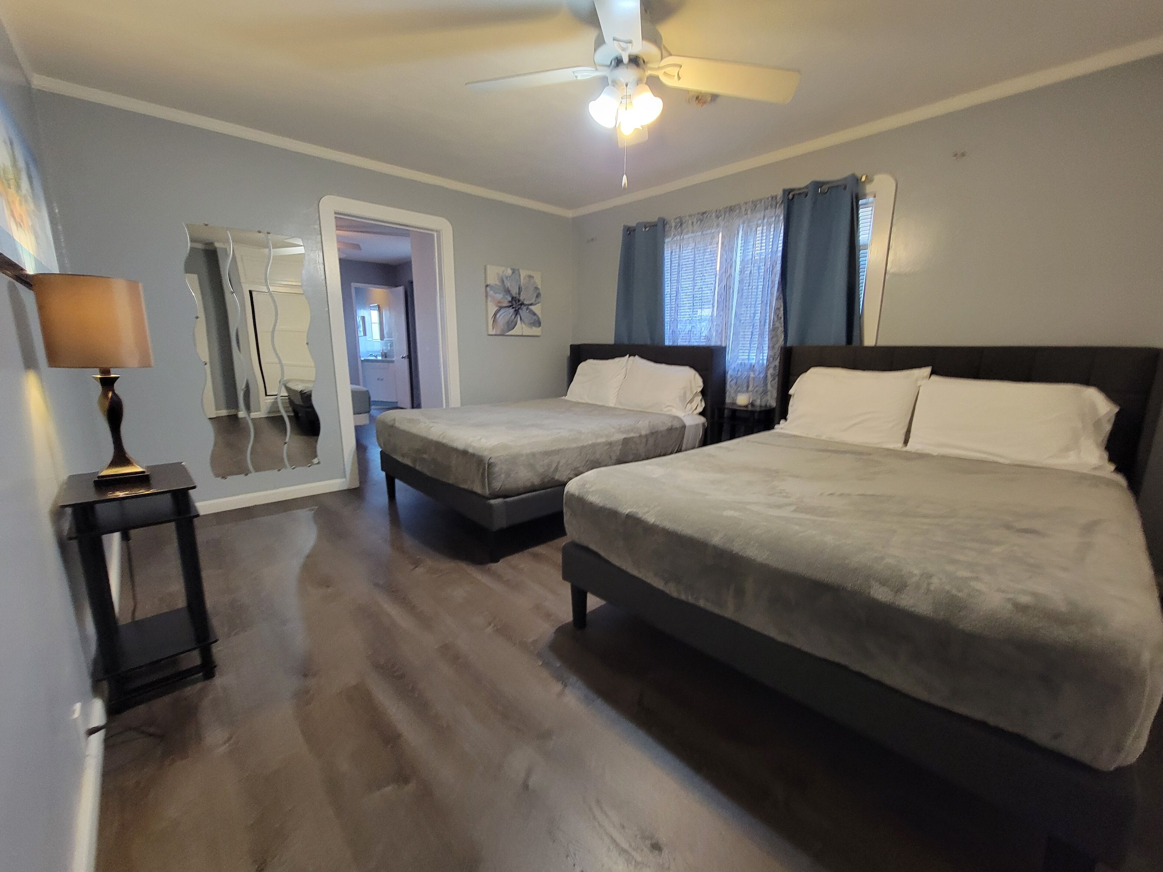 Habitación de hotel con dos camas, un ventilador de techo, una lámpara y vista al pasillo.