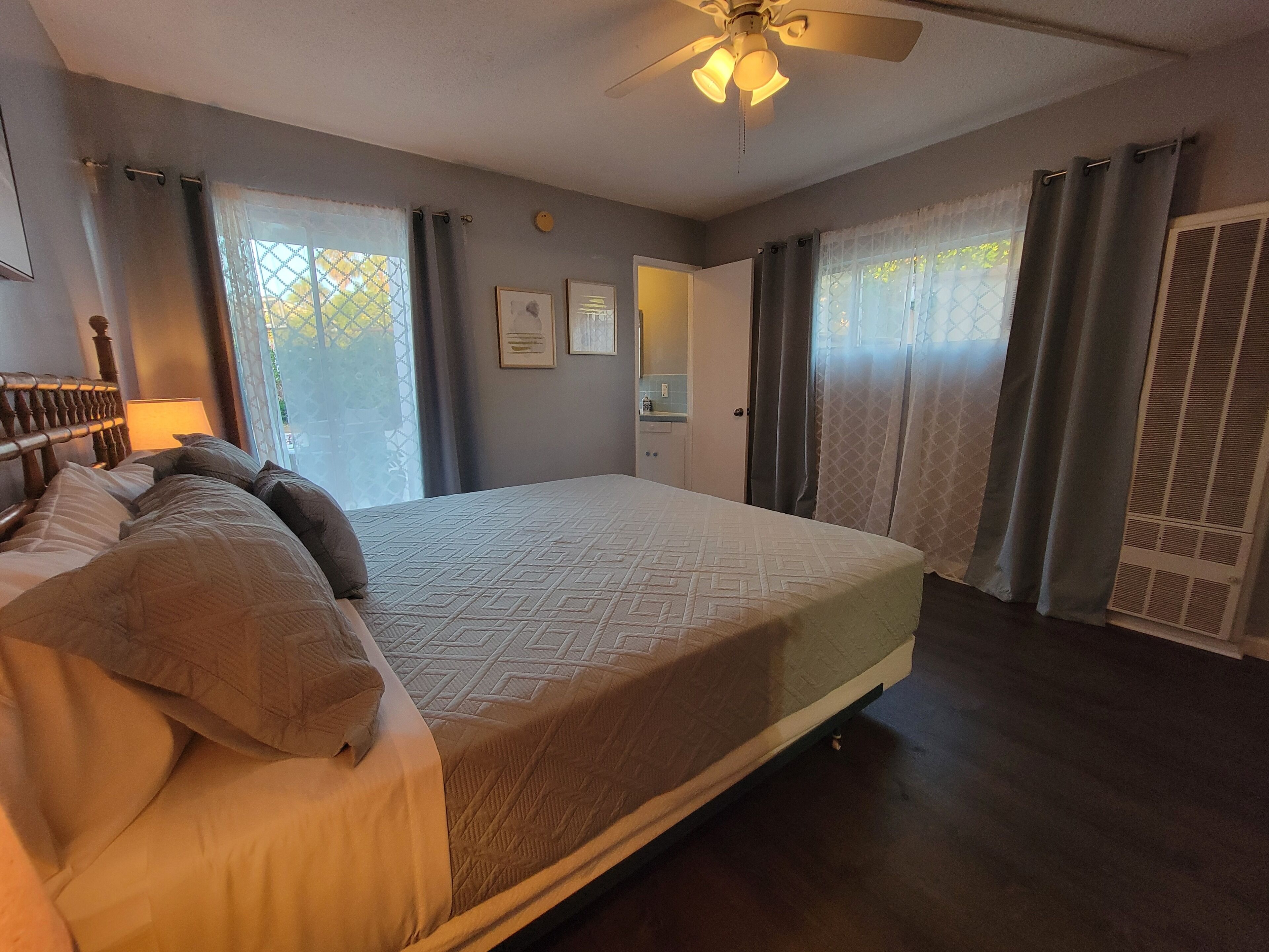 Een slaapkamer met een bed, een plafondventilator, een raam met gordijnen en een deur.
