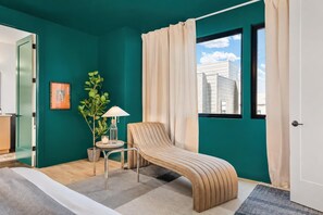 Una habitación moderna con paredes color turquesa, un banco curvo, una mesita con lámpara y una ventana con cortinas.