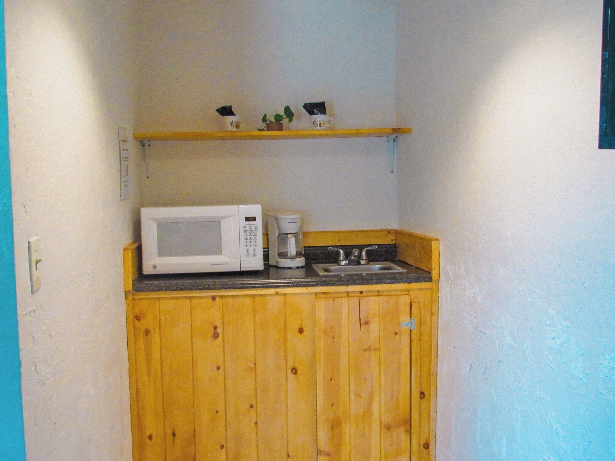 Une petite cuisine équipée d’un four à micro-ondes, d’une machine à café et d’une petite étagère au-dessus du plan de travail.