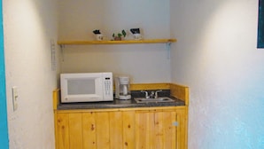 A compact kitchenette with a microwave, coffee maker, and a small shelf above the counter.