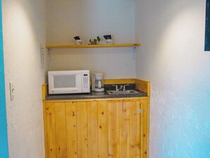 A compact kitchenette with a microwave, coffee maker, and a small shelf above the counter.