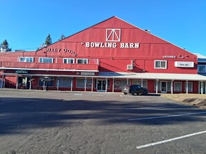 A red building with 'BOWLING BARN' signage, a storefront named 'ALLEY OOPS BISTRO,' and a car parked in front.