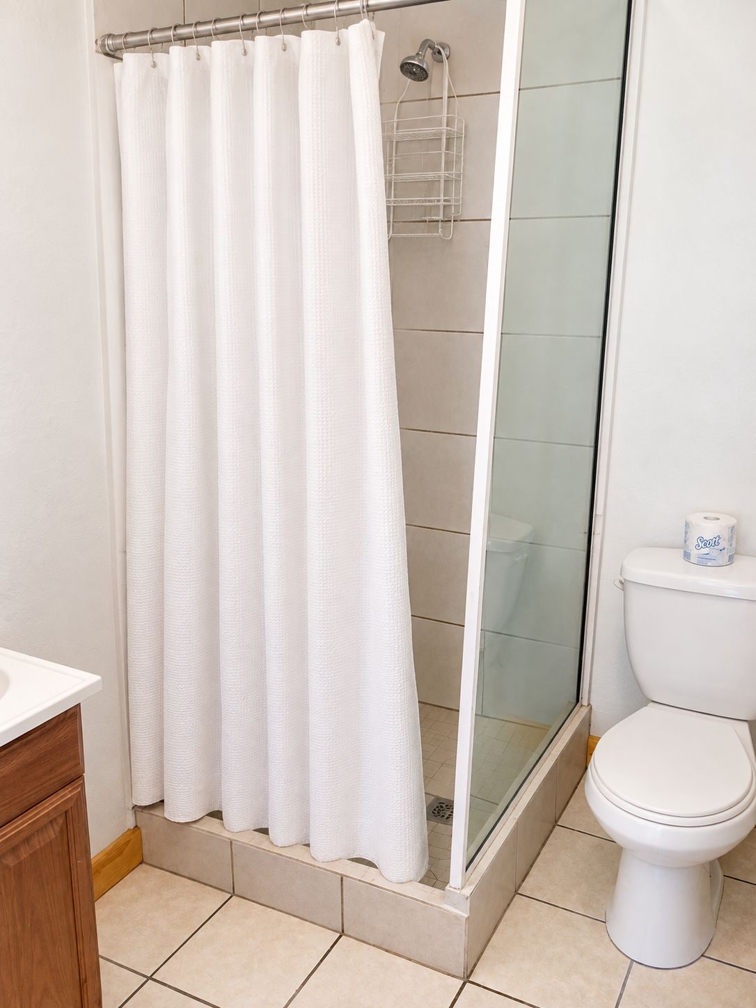 A bathroom with a shower curtain, a glass-enclosed shower, a toilet, and a wooden cabinet.