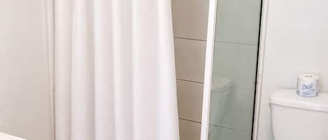 A bathroom with a shower curtain, a glass-enclosed shower, a toilet, and a wooden cabinet.