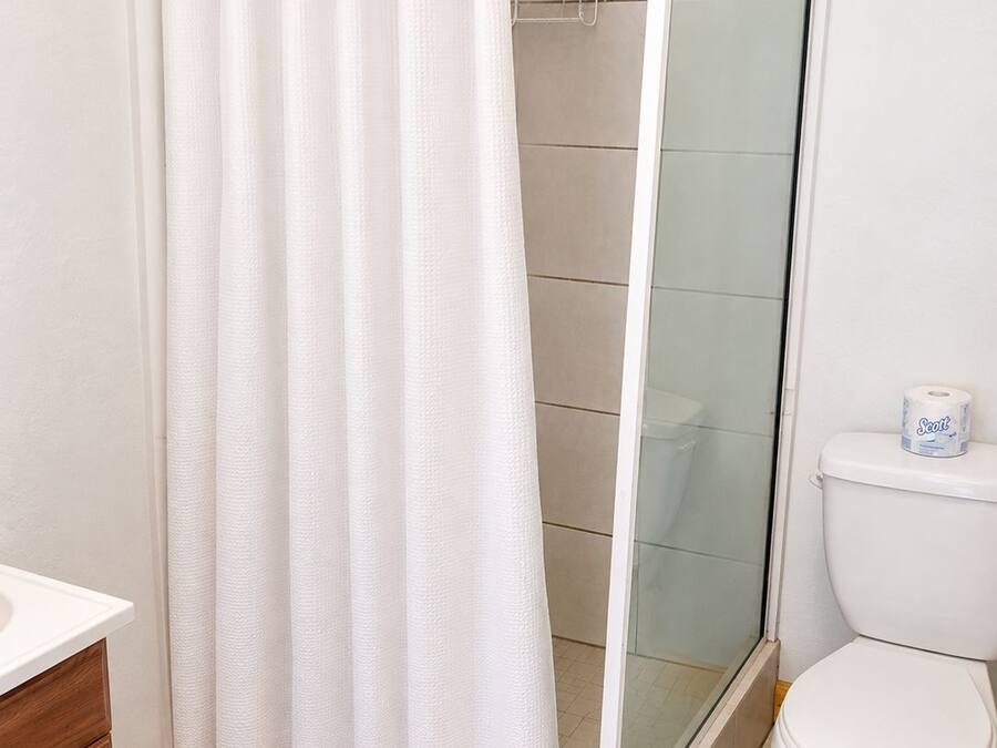 Een badkamer met douchegordijn, een douche met glazen wanden, een toilet en een houten kastje.