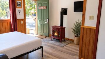 A cabin interior with a bed, a wood-burning stove, a green door labeled 'Cabin 42', and a view of the outside.