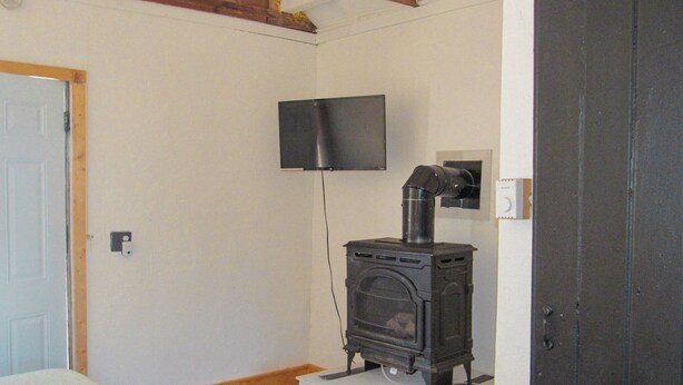 A room with a wood-burning stove, a television mounted on the wall, and a door.