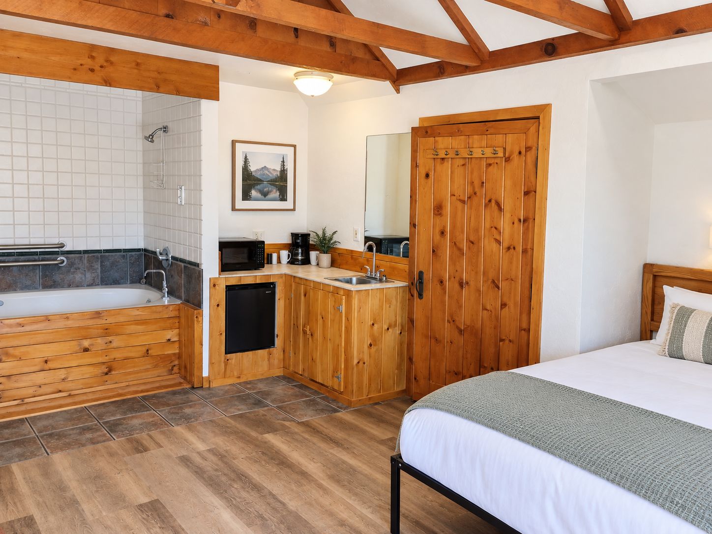 A bedroom with a wooden bed, a small kitchenette, a bathroom with a bathtub, and a wooden wardrobe.