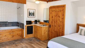 A bedroom with a wooden bed, a small kitchenette, a bathroom with a bathtub, and a wooden wardrobe.