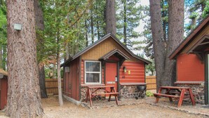 A cabin with a stone foundation, a red door, and a window. There are picnic tables in front.