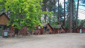 A campground with multiple cabins, picnic tables, and a gravel ground.