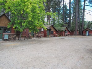 A campground with multiple cabins, picnic tables, and a gravel ground.
