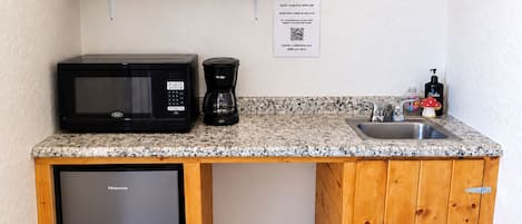Una kitchenette compacta con microondas, cafetera y lavamanos.