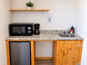 A compact kitchenette with a microwave, coffee maker, and sink.