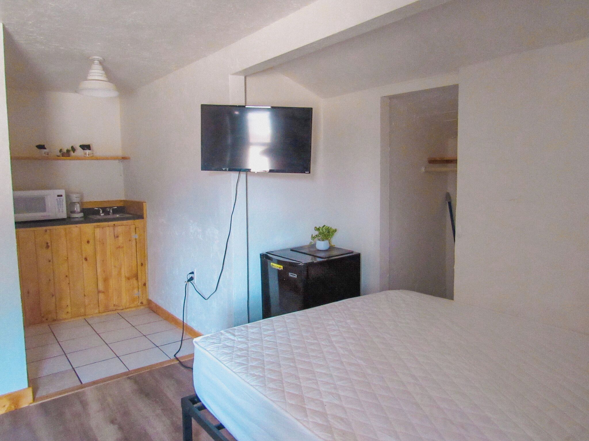 Une chambre de taille modeste comprenant un lit, une petite kitchenette, un téléviseur fixé au mur et un réfrigérateur.