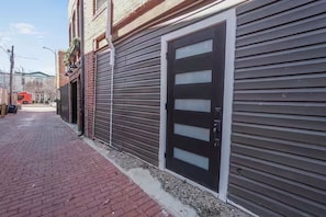 A building with a closed shutter door and a brick-paved walkway. - Cozy 1-bedroom carriage house on Capitol Hill with AC (Washington)
