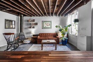 A cozy living room with a brown leather sofa, a wooden coffee table, a rocking chair, and a large potted plant. - Cozy 1-bedroom carriage house on Capitol Hill with AC (Washington)