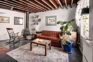 A cozy living room with a red sofa, a wooden coffee table, a rocking chair, and a large potted plant. - Cozy 1-bedroom carriage house on Capitol Hill with AC (Washington)