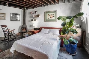 Ein gemütliches Schlafzimmer mit einem Bett, einem Schaukelstuhl, einem Kamin und einer großen Pflanze.