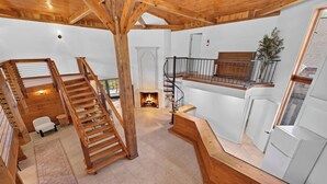 A spacious interior with a wooden staircase, a fireplace, and a balcony with a railing.