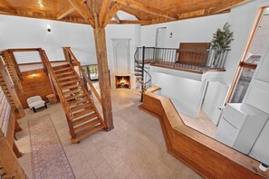 A spacious interior with a wooden staircase, a fireplace, and a balcony with a railing.