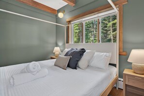 A bedroom with a large bed, a window with a view of trees, and a nightstand with a lamp.