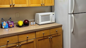 A kitchen with wooden cabinets, a white refrigerator, a microwave, and various food items on the counter.