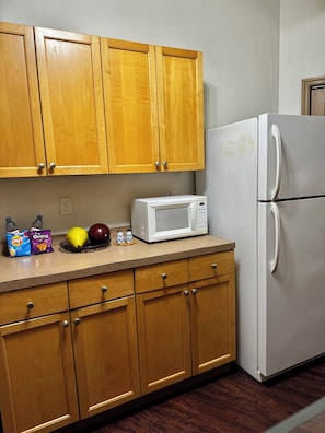 Una cocina con armarios de madera, un refrigerador blanco, un microondas y varios alimentos sobre la encimera.