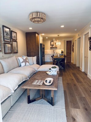 A modern living room with a sectional sofa, a coffee table, and a dining area with a wooden table and chairs. - Newly renovated 2-bedroom condo in lovely Hilton Head Island with AC (Hilton Head Island)