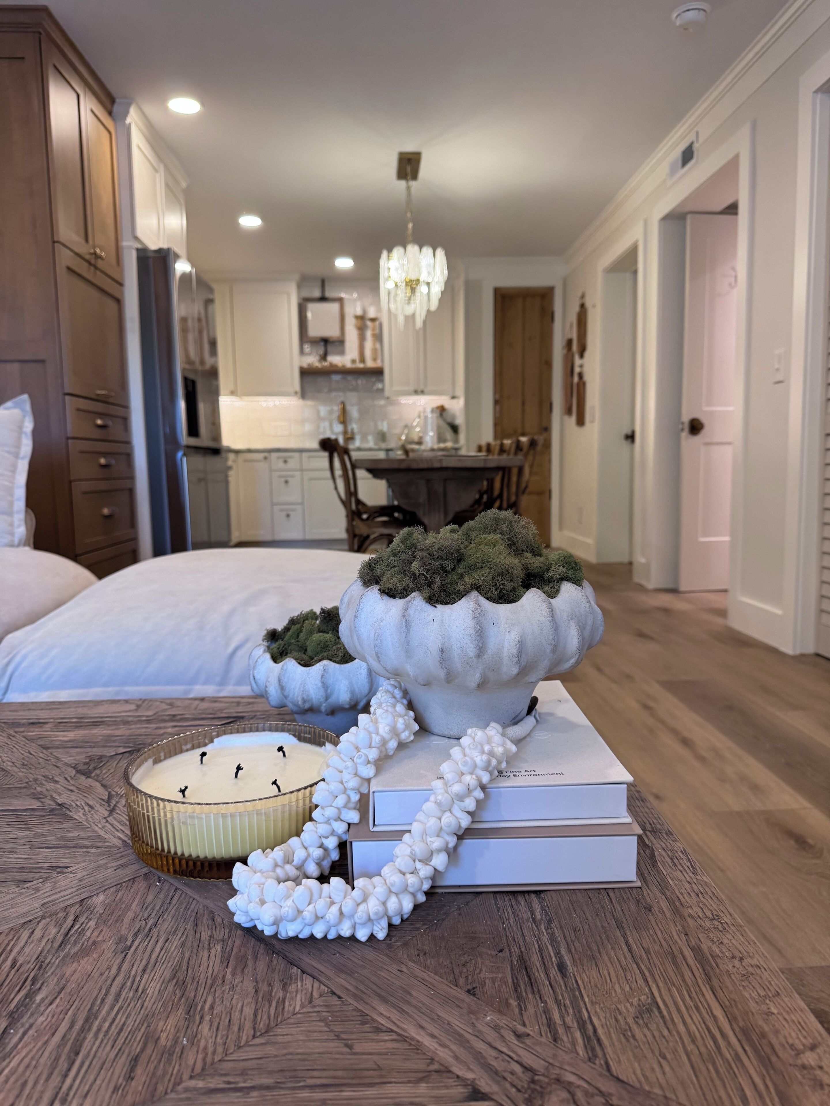 A bedroom with a bed, bedside table, and a decorative arrangement including a book, a string of pearls, and a small potted plant.