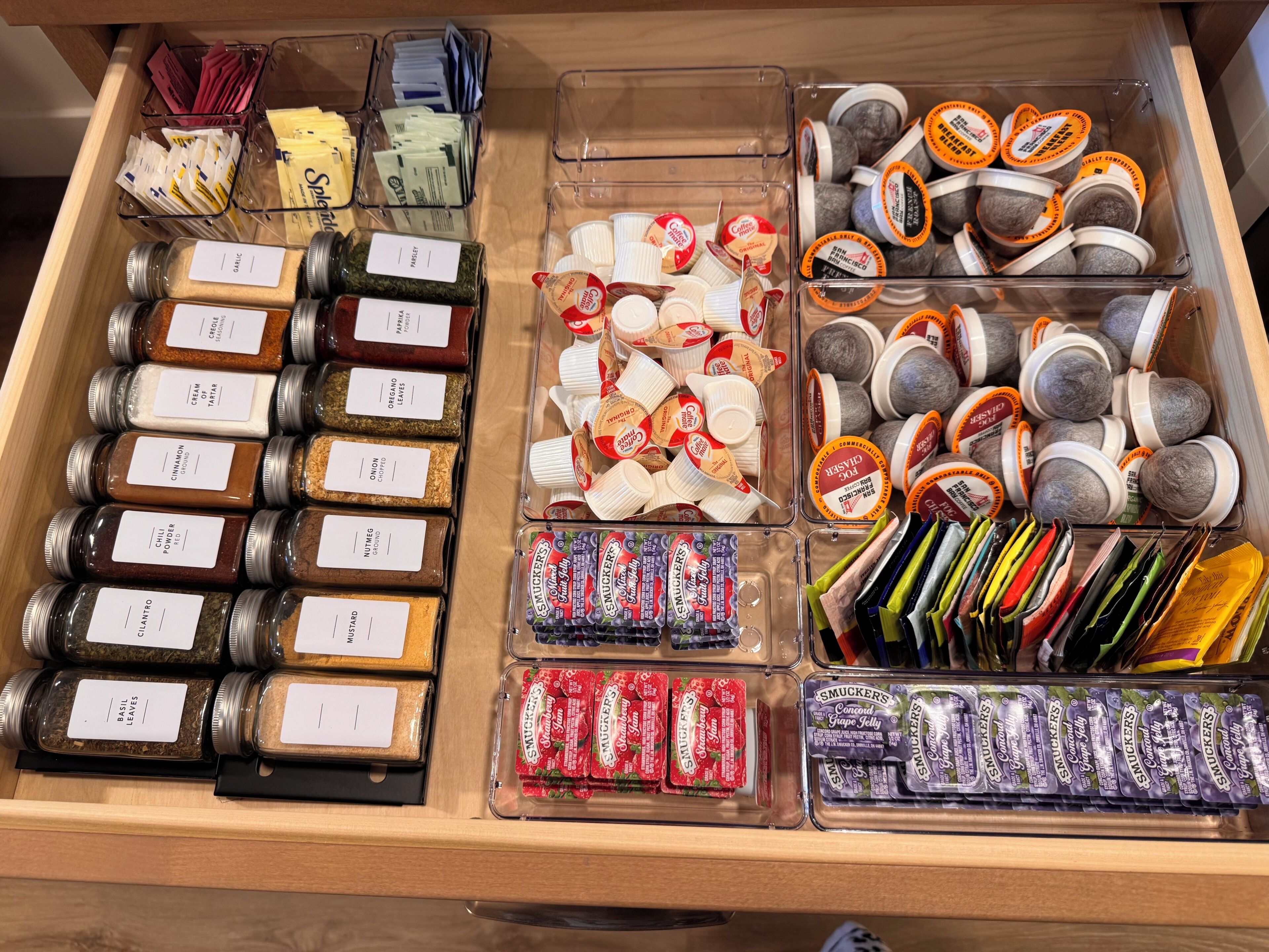 A drawer with various food items including jars of spices, packets of snacks, and containers of coffee.