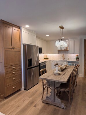 A modern kitchen with wooden cabinets, stainless steel appliances, a wooden dining table, and a chandelier. - Newly renovated 2-bedroom condo in lovely Hilton Head Island with AC (Hilton Head Island)
