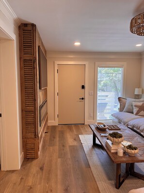A room with a wooden floor, a sofa, a coffee table, and a door with a television on the wall. - Newly renovated 2-bedroom condo in lovely Hilton Head Island with AC (Hilton Head Island)