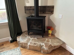 A stone fireplace with a black stove, a vase with flowers, and a window with curtains. - The Historic Sugar Mill House with Hot Tub (Loveland)