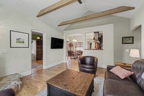 A living room with a wooden coffee table, leather sofa, and a dining area in the background. - The Historic Sugar Mill House with Hot Tub (Loveland)