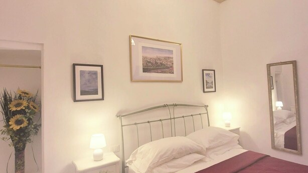 A bedroom with a bed, a nightstand, a mirror, and a window with a view. - Lady Flor B&B (Firenze)