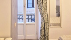 A bedroom with a double door, a bed, a bedside table, a mirror, and a window with a view of the outside. - Lady Flor B&B (Firenze)
