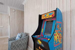 Ein Zimmer mit einem Vintage-Pac-Man-Arcade-Spiel, einem gemusterten Sessel und Holzvertäfelung an den Wänden.