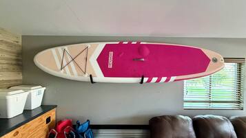 A ceiling-mounted surfboard with a pink and white design, a wooden cabinet with storage bins, and a brown leather couch.