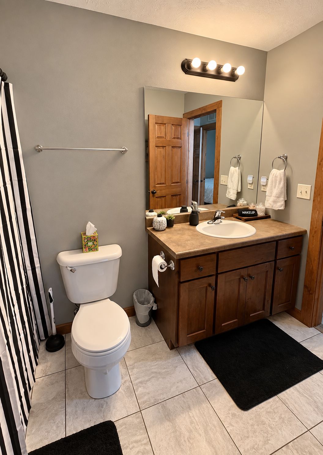 A bathroom with a toilet, sink, vanity, and a mirror.